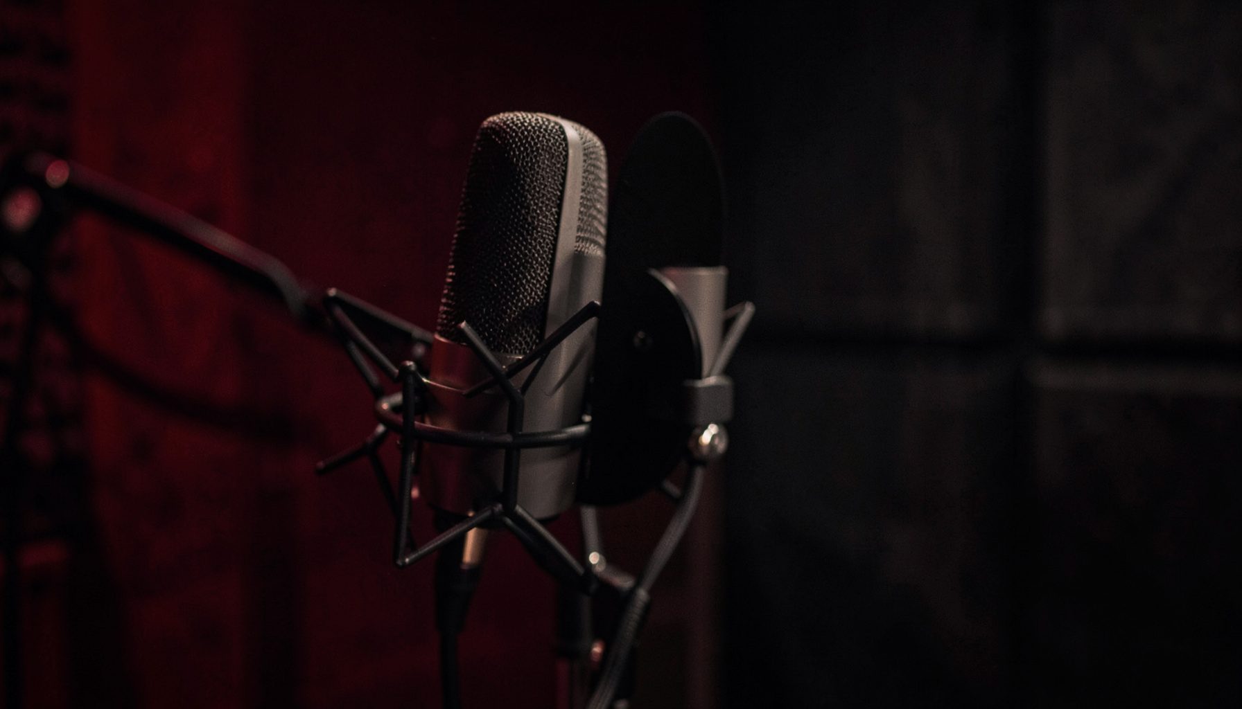 Close-up of a microphone in a softly lit studio booth, deep red and charcoal tones, moody and intimate