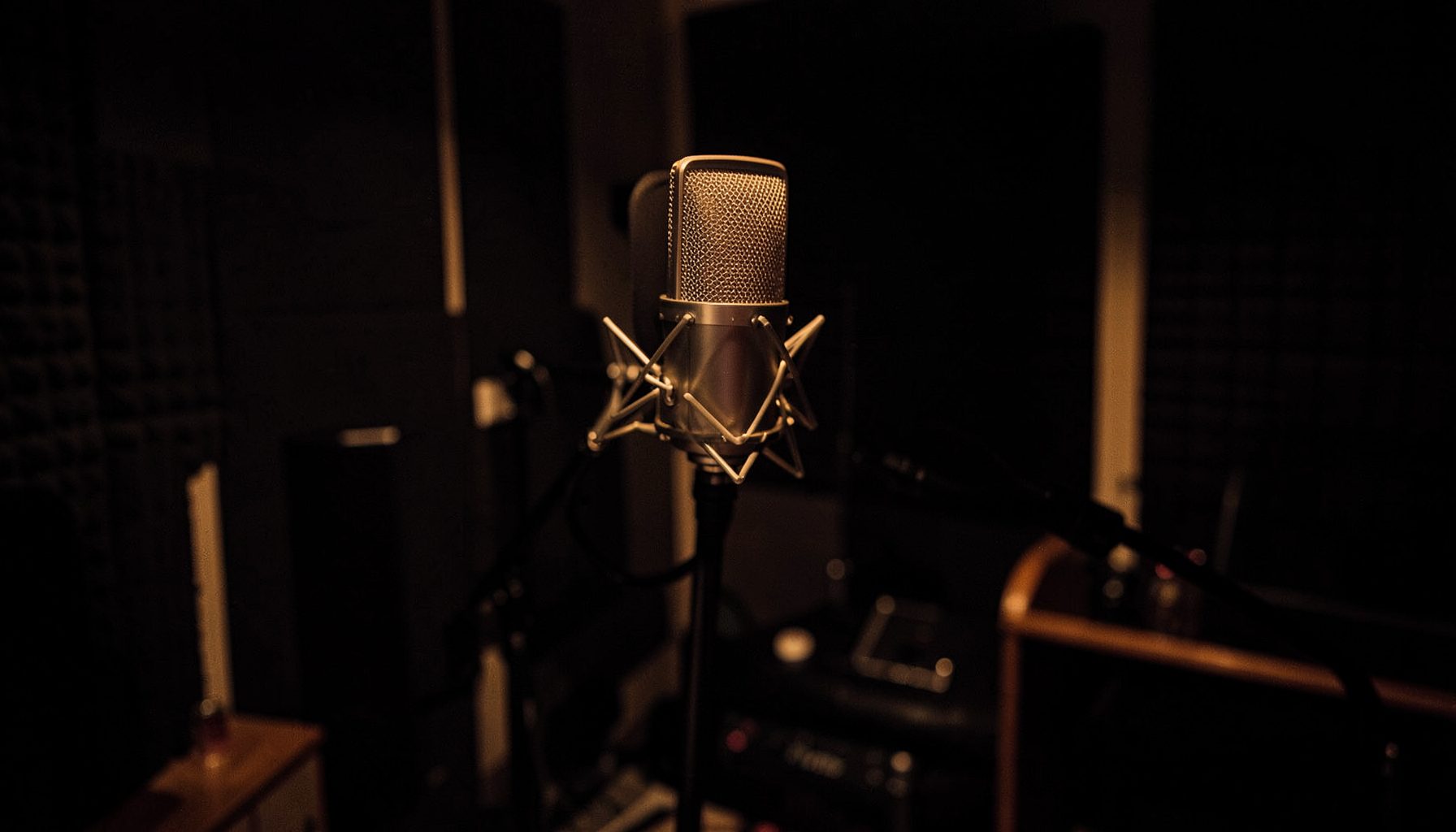Dimly lit recording studio with microphone on a stand, warm amber and deep shadow tones
