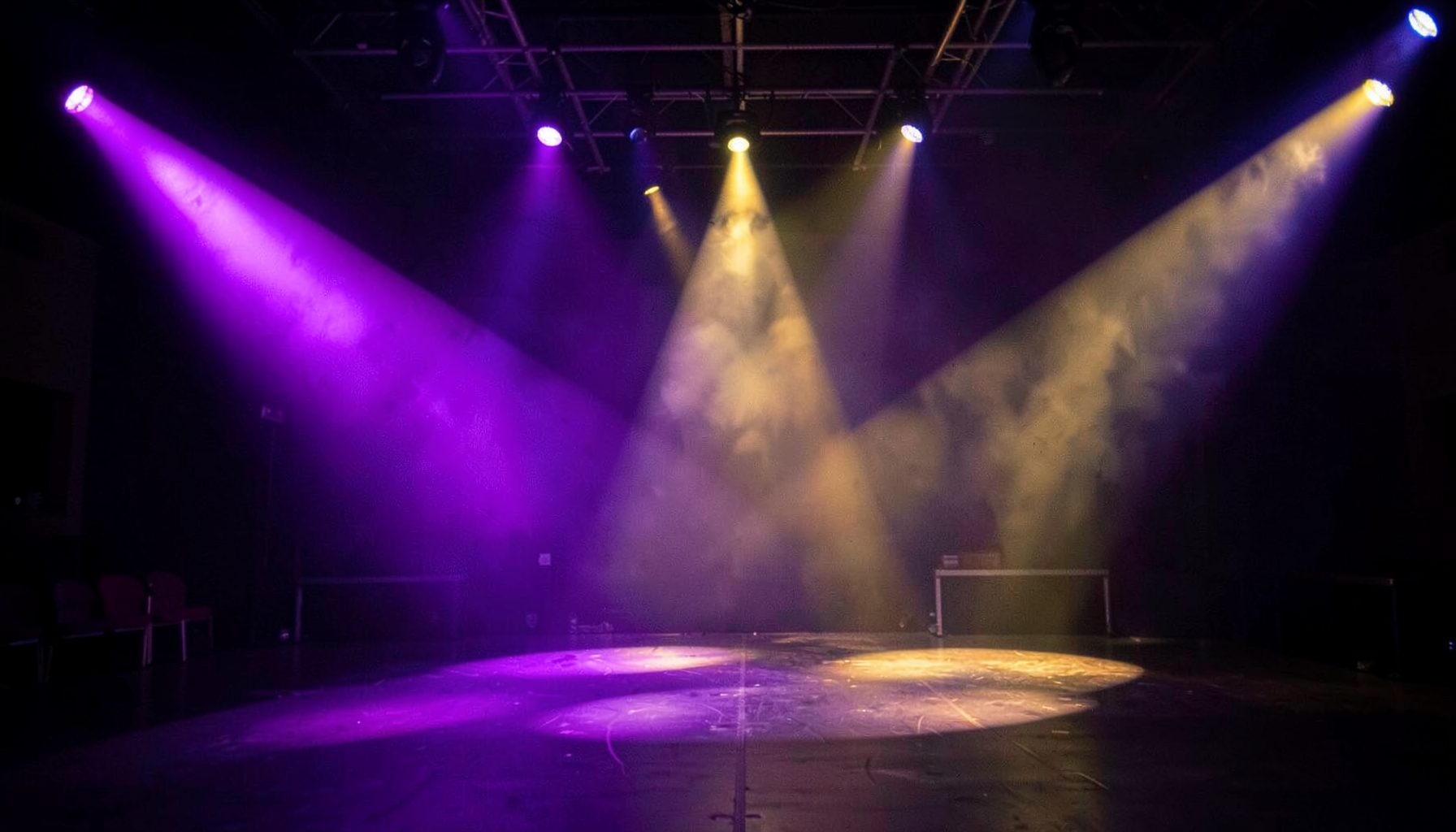 Stage lighting casting dramatic purple and gold beams across an empty venue, anticipation and energy